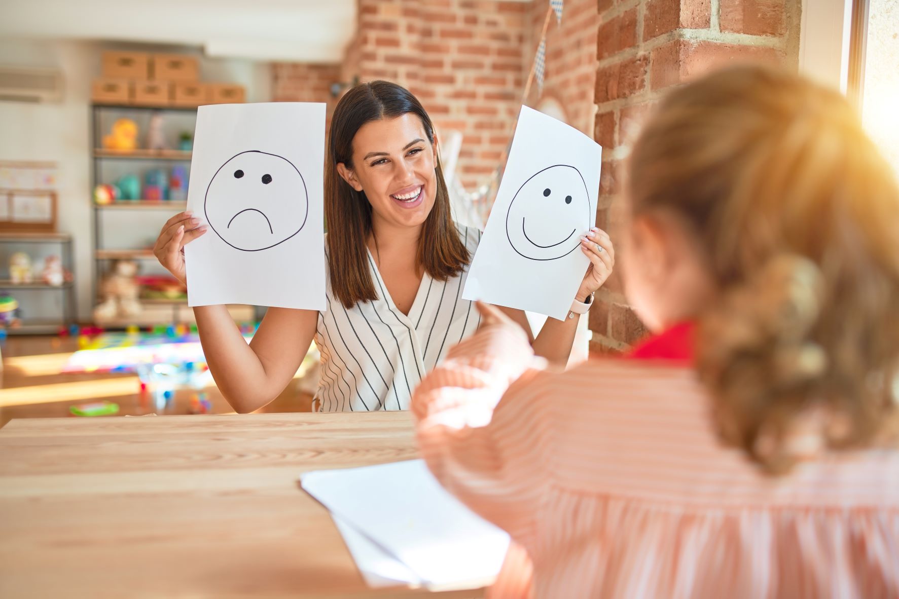 Eine Frau hält in der linken Hand ein Blatt Papier mit einem fröhliche Smiley, während sie in der rechten Hand ein Blatt mit einem traurigen Smiley hochhält.