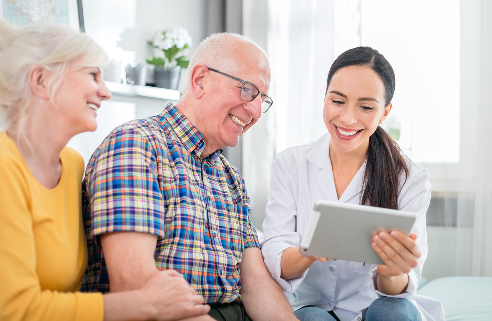 Eine Frau mit Tablet erklärt einem älteren Ehepaar etwas auf dem Bildschirm